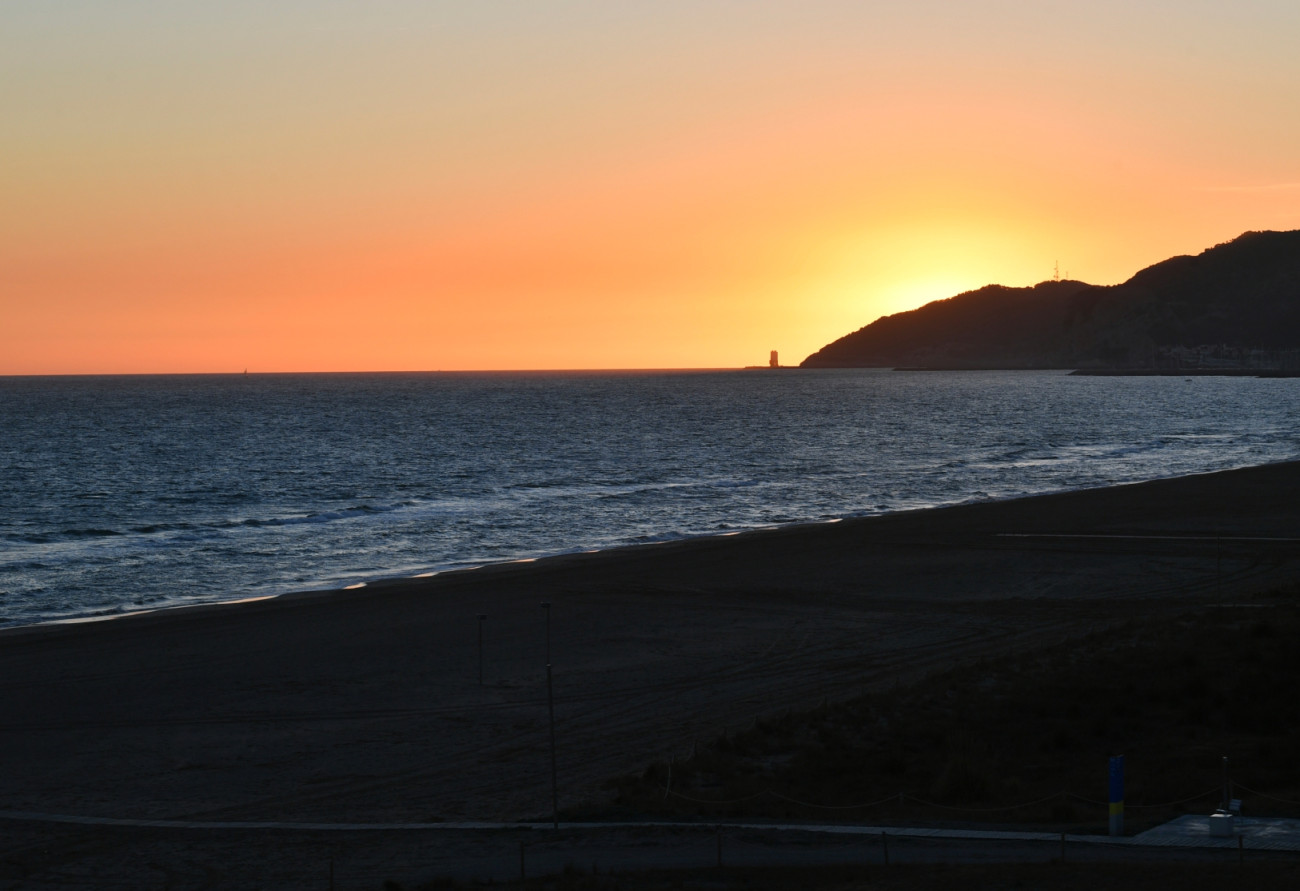 Vista de la costa de Castelldefels al capvespre, amb el mar i el perfil del litoral retallats per l’última llum del dia.