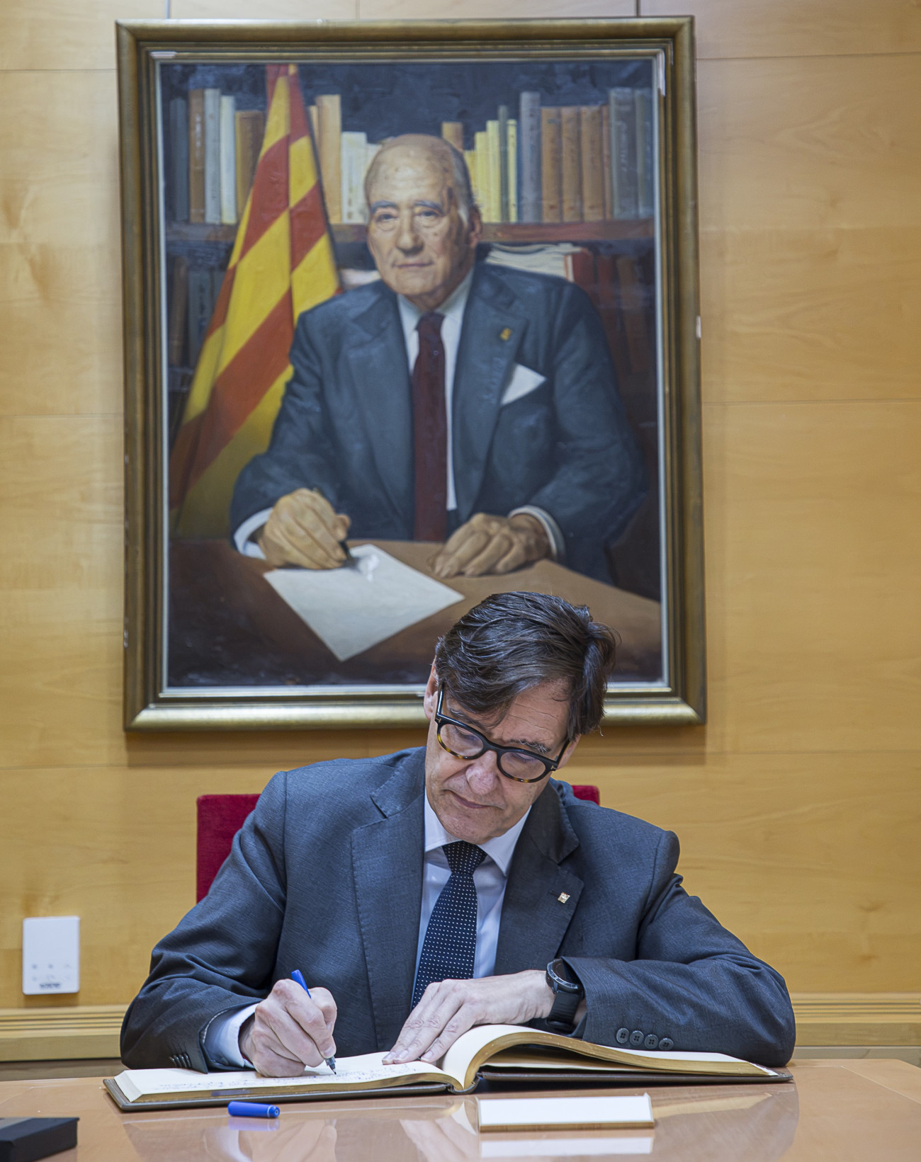 El president Salvador Illa signa el llibre d’autoritats sota el quadre del també president Josep Tarradellas, que presideix una de les sales de l’Ajuntament de Cervelló.